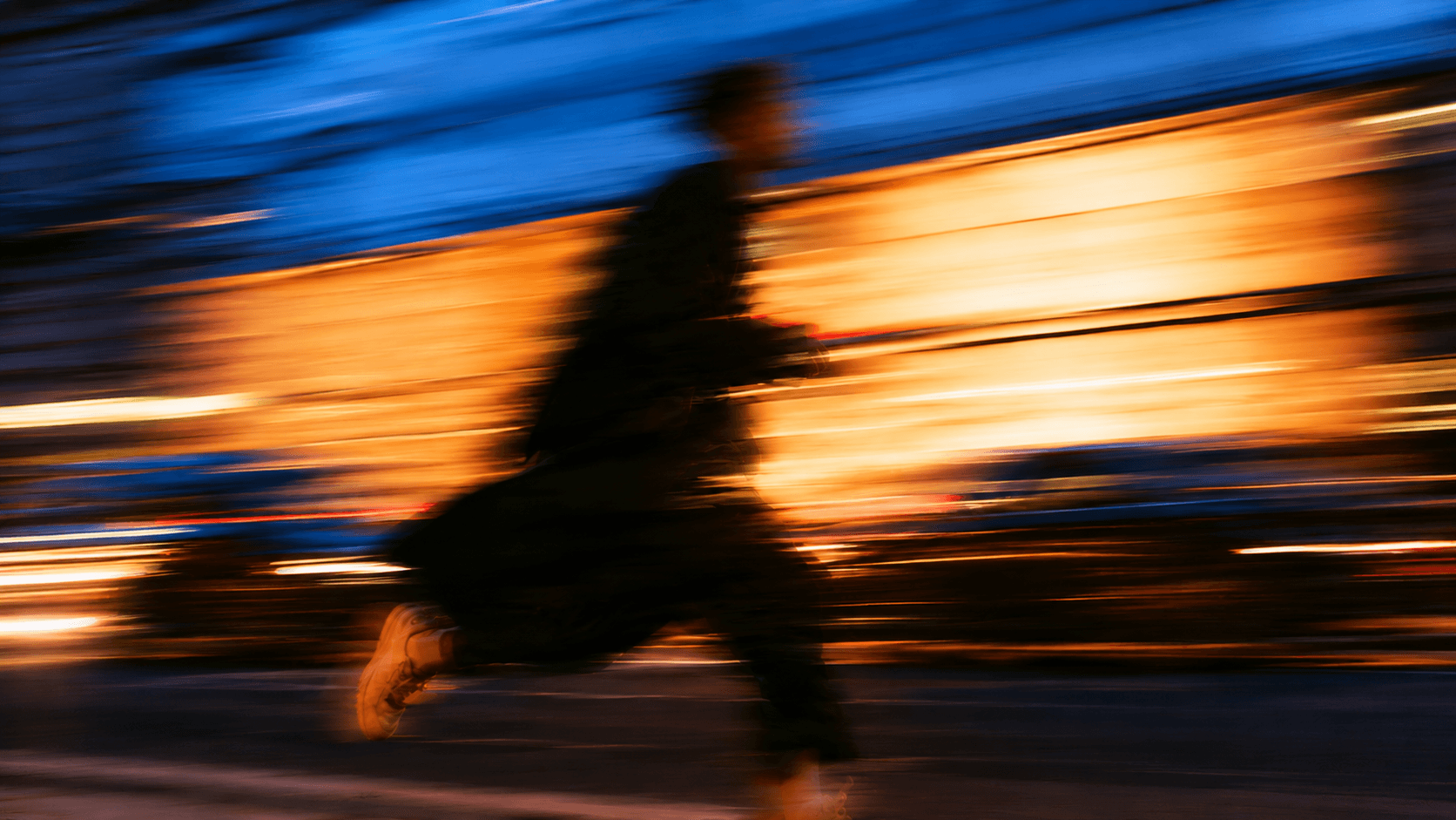 Motion-blurred photograph of a figure running past city light at dusk